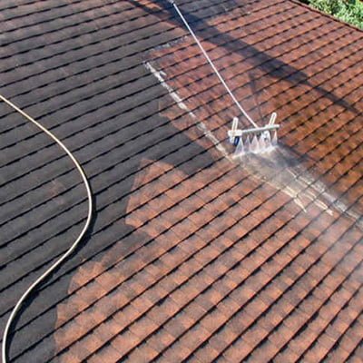 A soft washer cleaning a dirty, shingled roof, showing a clear line between the cleaned and uncleaned sections.